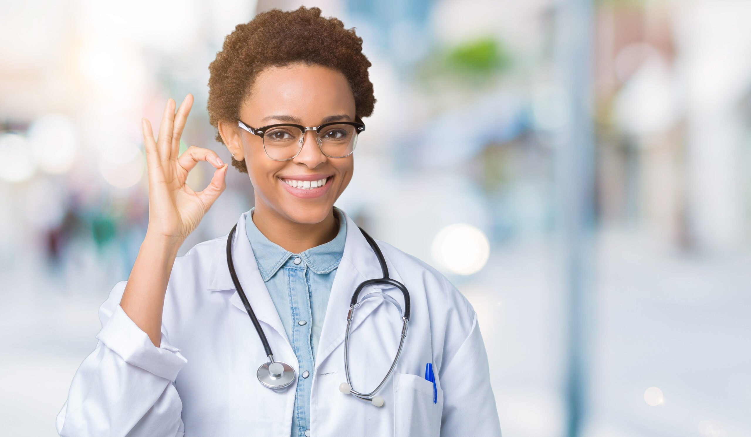 Young african american doctor woman wearing medical coat over isolated background smiling positive doing ok sign with hand and fingers. Successful expression.
