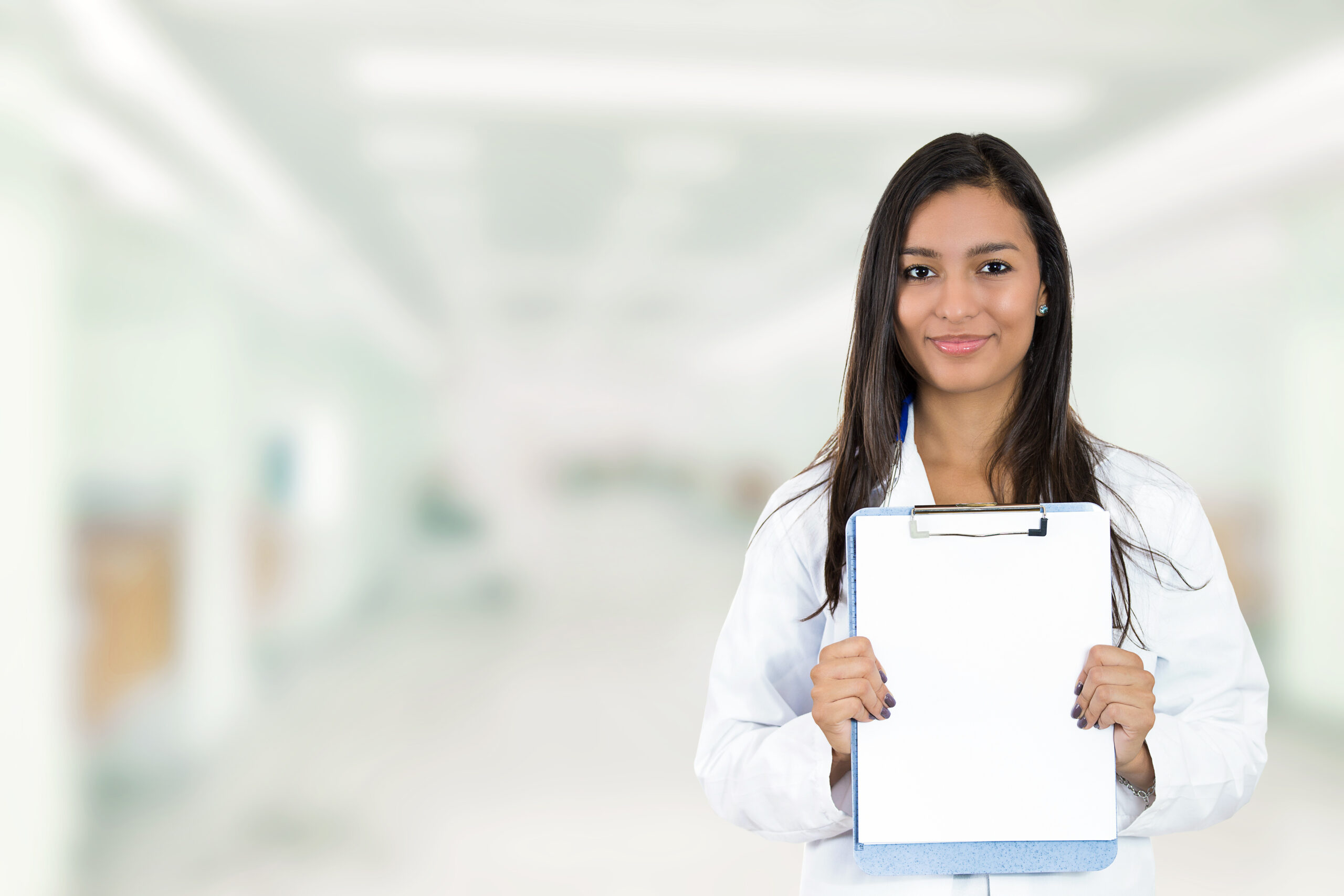 Happy smiling doctor holding clipboard standing in hospital hallway isolated on clinic windows background